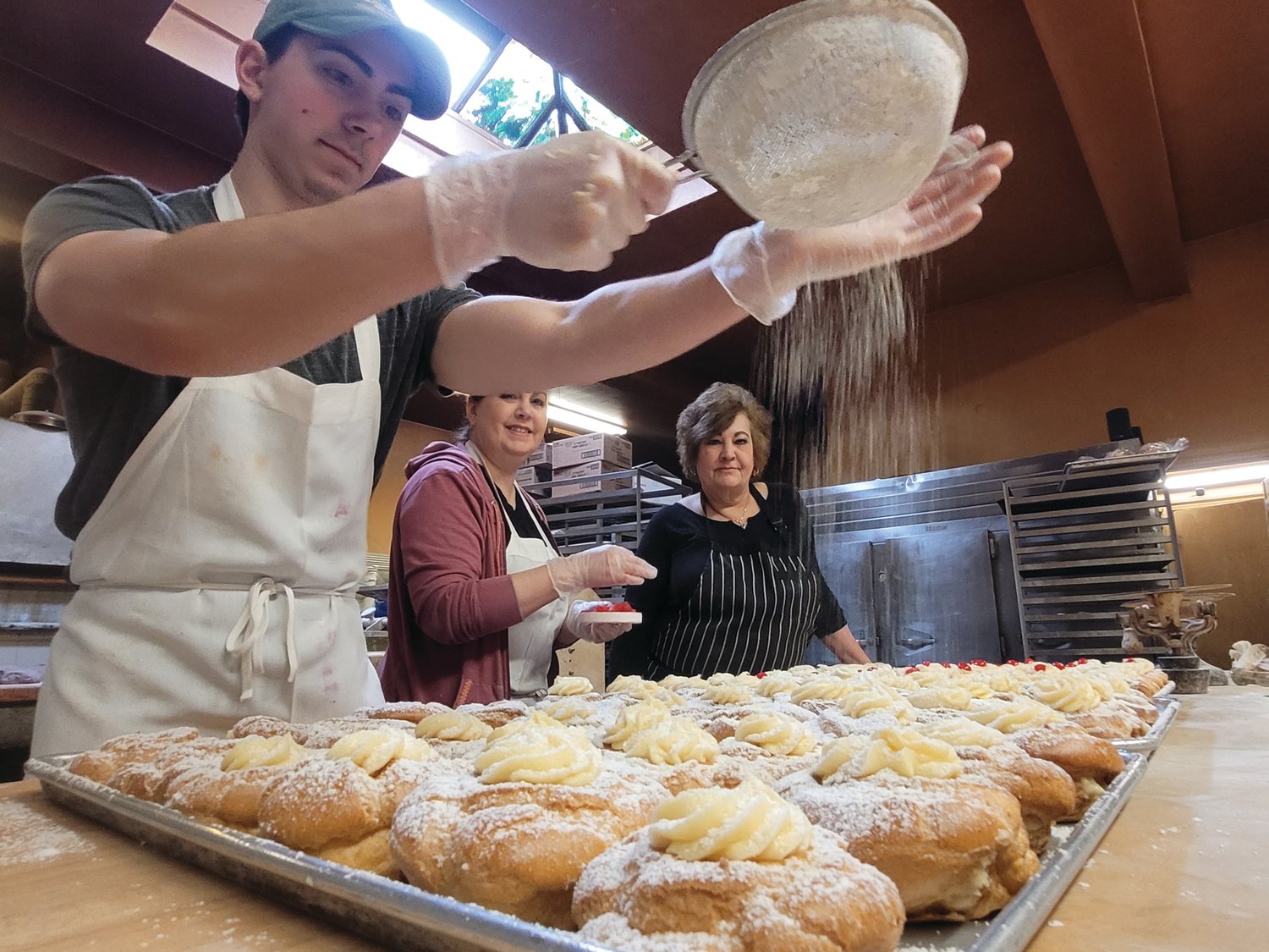A DUSTING OF TRADITION: Brendan Notarianni shakes some sugar on a completed batch of zeppoles, as his mother Diane Notarianni, and aunt, Paula Arlia, watch on.